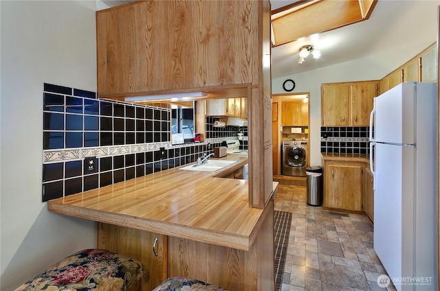 kitchen featuring a peninsula, freestanding refrigerator, stone finish flooring, tasteful backsplash, and washer / dryer