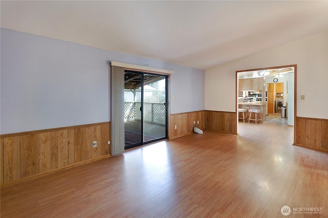 spare room with a wainscoted wall, vaulted ceiling, and wood finished floors