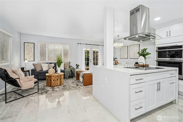 kitchen featuring open floor plan, double oven, light countertops, island range hood, and white cabinetry