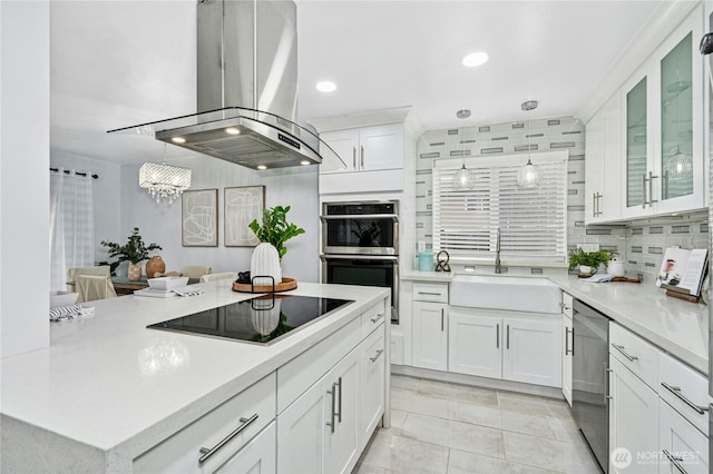 kitchen featuring light countertops, appliances with stainless steel finishes, island range hood, white cabinetry, and a sink