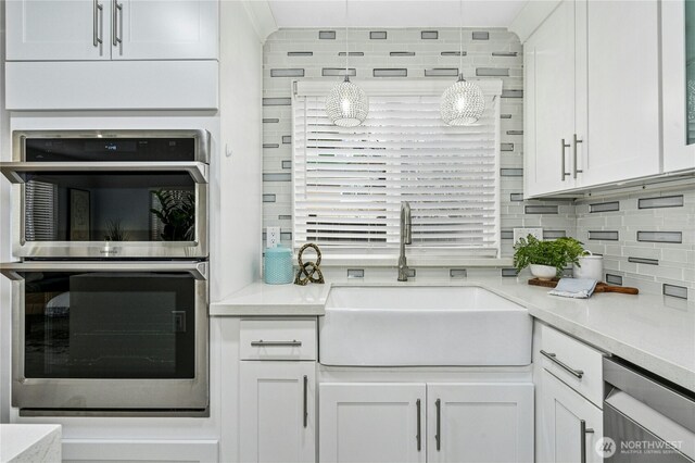 kitchen featuring a sink, backsplash, appliances with stainless steel finishes, white cabinets, and light countertops