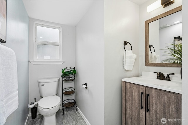 half bathroom with vanity, toilet, and baseboards