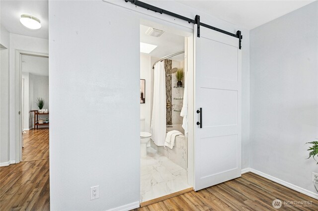 interior space with a barn door, wood finished floors, baseboards, and visible vents