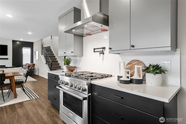 kitchen with wall chimney exhaust hood, dark wood finished floors, high end range, and light countertops