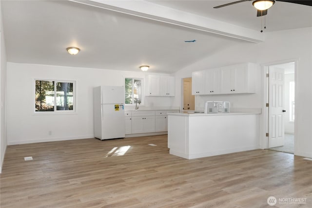 kitchen with vaulted ceiling with beams, light countertops, freestanding refrigerator, white cabinetry, and light wood-type flooring