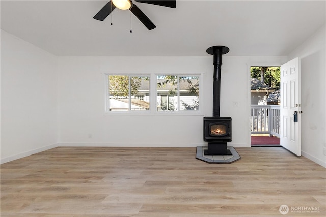 unfurnished living room with a wood stove, light wood finished floors, ceiling fan, and baseboards