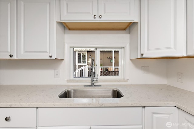 kitchen with light stone countertops, white cabinets, and a sink