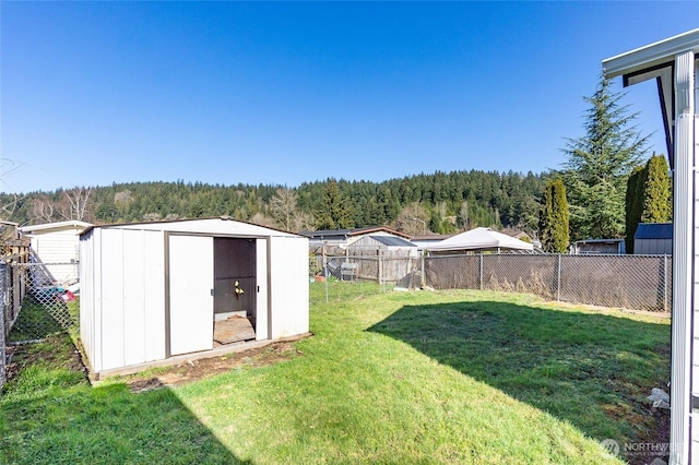 view of yard featuring an outbuilding, a fenced backyard, a wooded view, and a storage shed