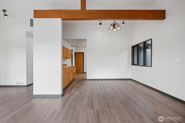 unfurnished room with baseboards, visible vents, beamed ceiling, and wood finished floors