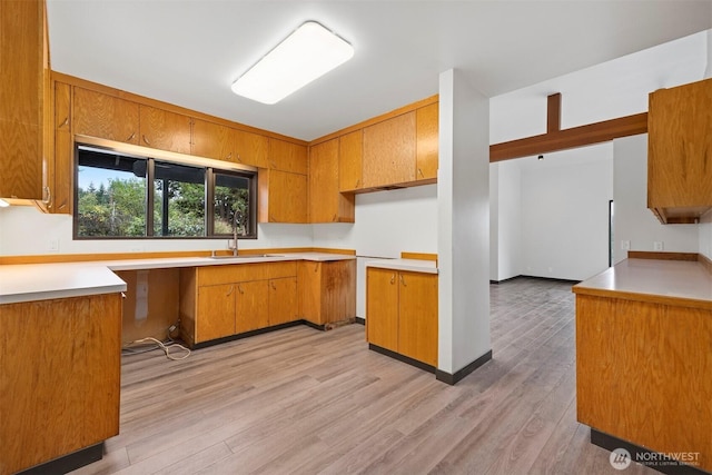 kitchen featuring brown cabinetry, light wood-type flooring, light countertops, and a sink