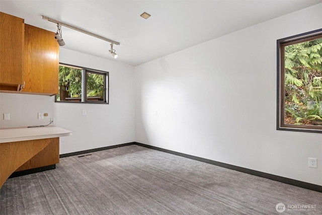 kitchen with carpet, brown cabinets, light countertops, track lighting, and baseboards