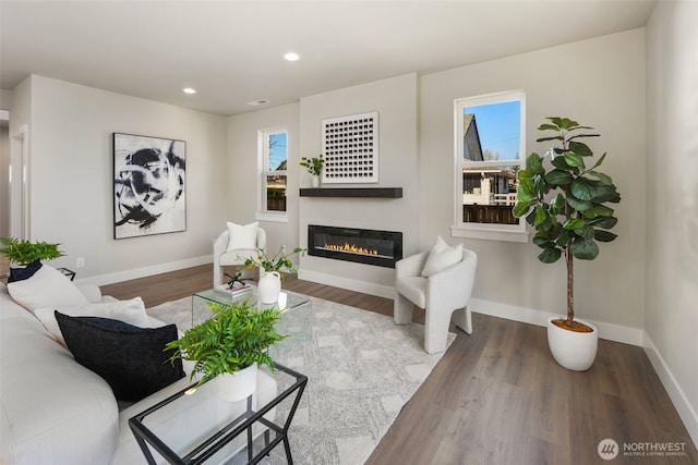 living room featuring a glass covered fireplace, recessed lighting, baseboards, and wood finished floors