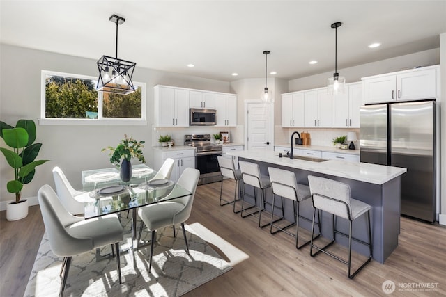 kitchen featuring a breakfast bar, stainless steel appliances, light wood-style floors, white cabinetry, and a sink