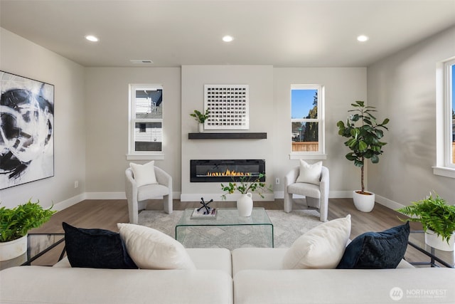 living room with plenty of natural light, visible vents, wood finished floors, and a glass covered fireplace