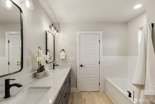 full bath featuring a garden tub, double vanity, wood finished floors, and a sink