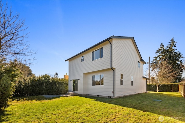 back of house with entry steps, a lawn, and fence