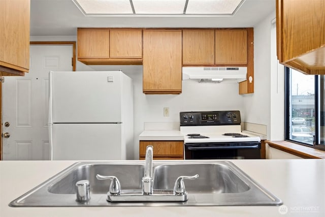 kitchen featuring electric stove, light countertops, freestanding refrigerator, a sink, and under cabinet range hood