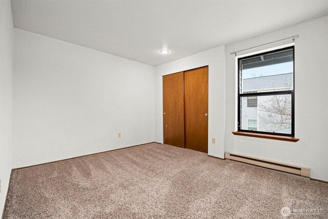 unfurnished bedroom with a baseboard heating unit, a closet, and carpet