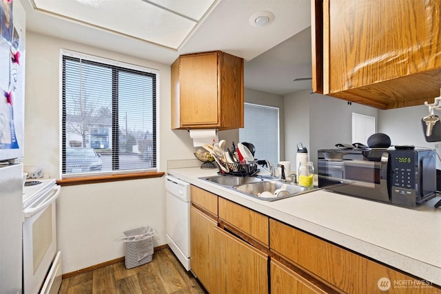 kitchen featuring white appliances, baseboards, wood finished floors, light countertops, and a sink