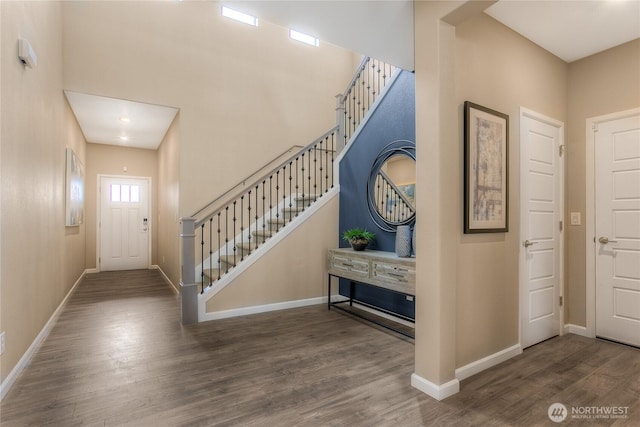 foyer with a towering ceiling, baseboards, stairway, and wood finished floors