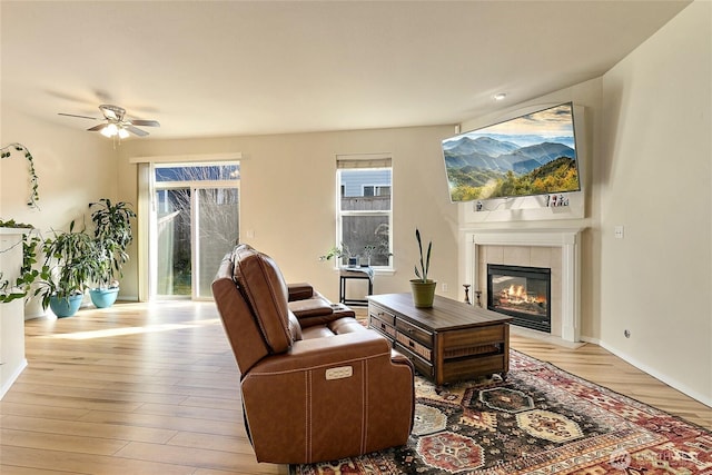 living room featuring a ceiling fan, a tiled fireplace, and light wood finished floors