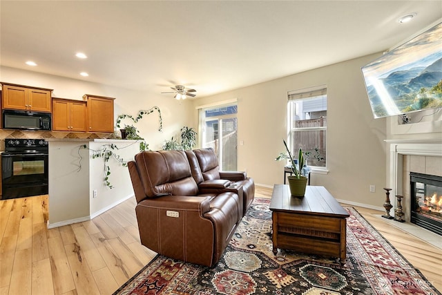 living area featuring a tile fireplace, recessed lighting, a ceiling fan, baseboards, and light wood finished floors