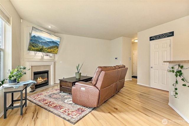 living area with a glass covered fireplace, baseboards, and light wood finished floors