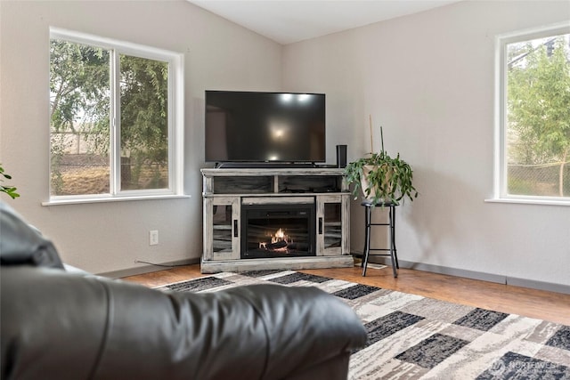 living room featuring a glass covered fireplace, baseboards, and wood finished floors