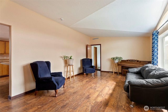 sitting room with visible vents, vaulted ceiling, baseboards, and wood finished floors