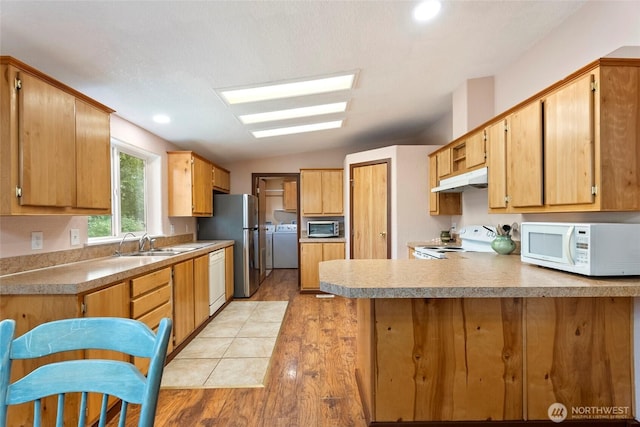 kitchen featuring appliances with stainless steel finishes, a peninsula, vaulted ceiling, under cabinet range hood, and a sink