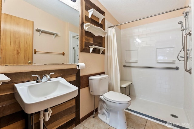 full bath featuring toilet, tile patterned flooring, a tile shower, and a sink