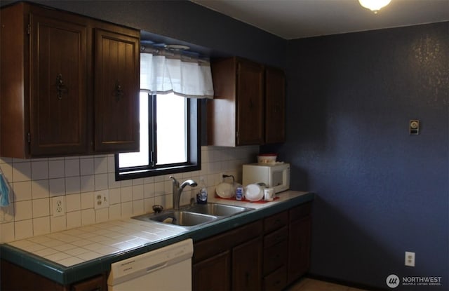 kitchen featuring dark brown cabinetry, white appliances, a sink, backsplash, and tile counters