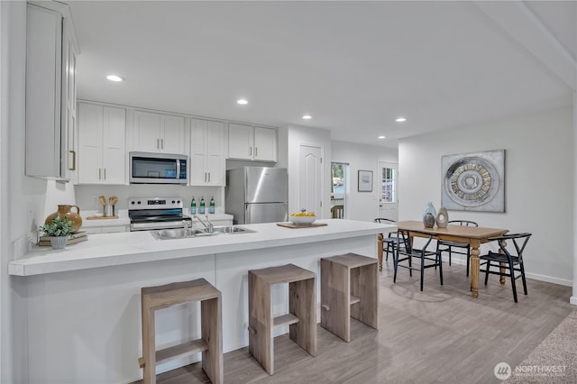 kitchen with light wood-style flooring, appliances with stainless steel finishes, a peninsula, a kitchen bar, and recessed lighting