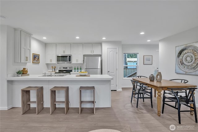 kitchen featuring appliances with stainless steel finishes, a kitchen breakfast bar, a peninsula, light countertops, and recessed lighting