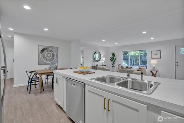 kitchen with white cabinets, light countertops, light wood-type flooring, stainless steel dishwasher, and a sink