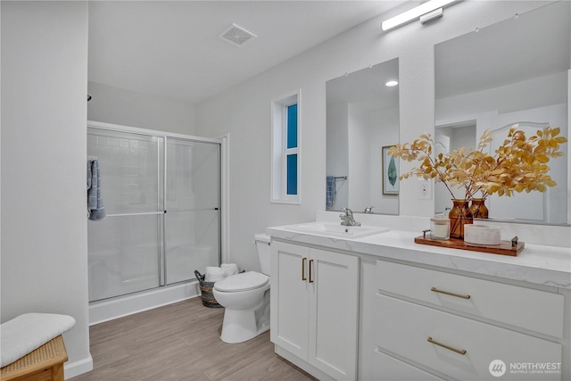 bathroom with visible vents, toilet, wood finished floors, vanity, and a shower stall