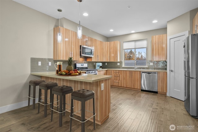 kitchen with stainless steel appliances, light wood-type flooring, a peninsula, and a sink