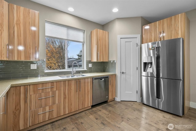 kitchen with light wood-type flooring, tasteful backsplash, appliances with stainless steel finishes, and a sink