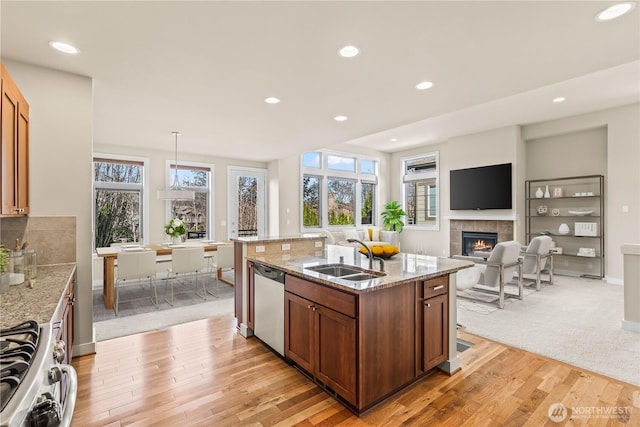 kitchen with a tile fireplace, a sink, stainless steel dishwasher, range, and light stone countertops