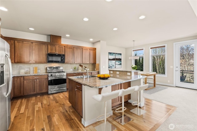 kitchen featuring light stone counters, backsplash, appliances with stainless steel finishes, a sink, and a kitchen breakfast bar