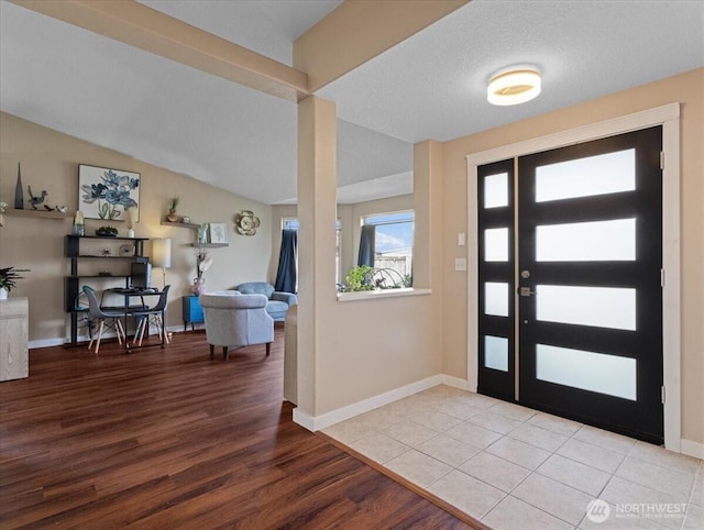 foyer entrance with baseboards, vaulted ceiling, and wood finished floors