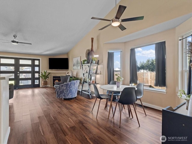 dining space featuring lofted ceiling, ceiling fan, wood finished floors, baseboards, and a lit fireplace