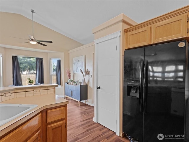 kitchen featuring lofted ceiling, light countertops, black refrigerator with ice dispenser, ceiling fan, and wood finished floors