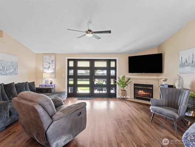 living area with vaulted ceiling, a tile fireplace, wood finished floors, and a ceiling fan