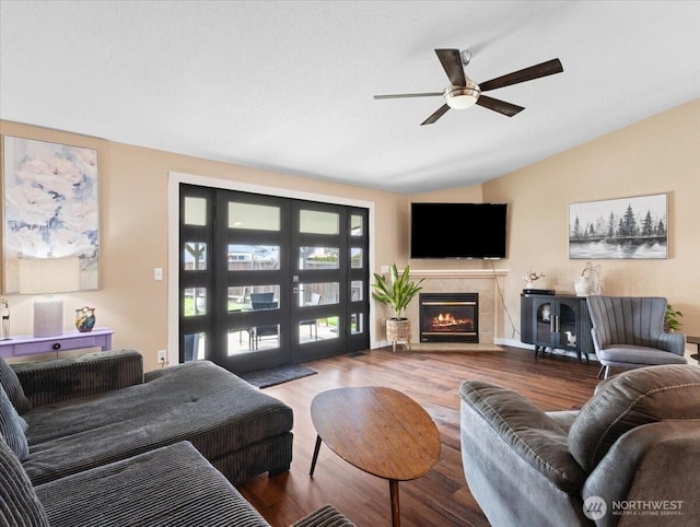 living area with lofted ceiling, a fireplace with flush hearth, wood finished floors, and a ceiling fan