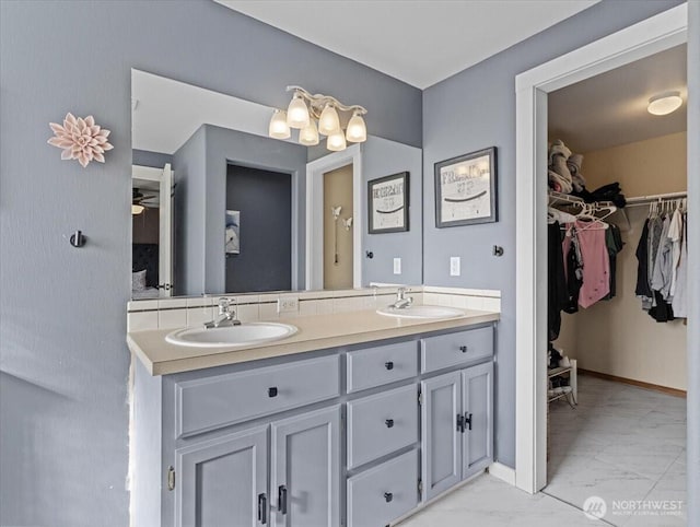 full bathroom featuring double vanity, marble finish floor, a spacious closet, and a sink