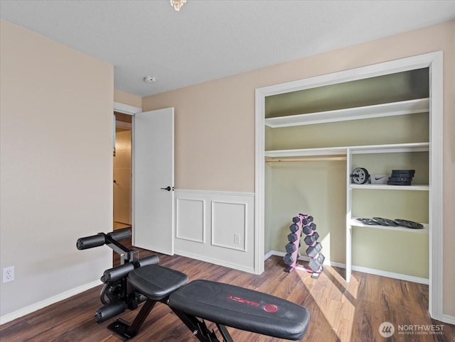 exercise area with a wainscoted wall, a decorative wall, baseboards, and wood finished floors