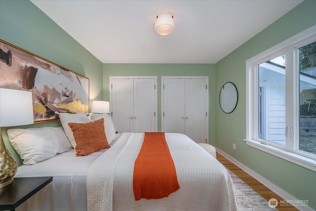 bedroom with wood finished floors, multiple windows, baseboards, and two closets