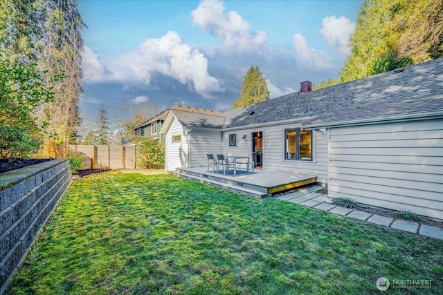 back of house with roof with shingles, a yard, a chimney, a deck, and a fenced backyard