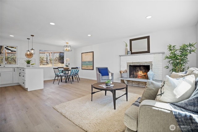 living room with a warm lit fireplace, light wood-style flooring, baseboards, and recessed lighting